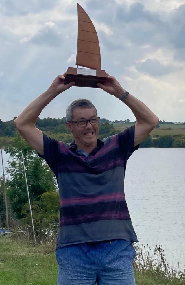 NHEBSC club member David holding a trophy above his head with the Blue Lagoon in the background.